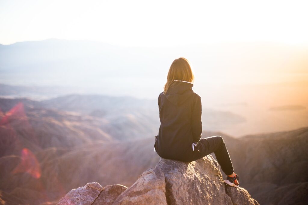 Vrouw kijkt bij zonsopkomst uit over het landschap, klaar voor een nieuwe start